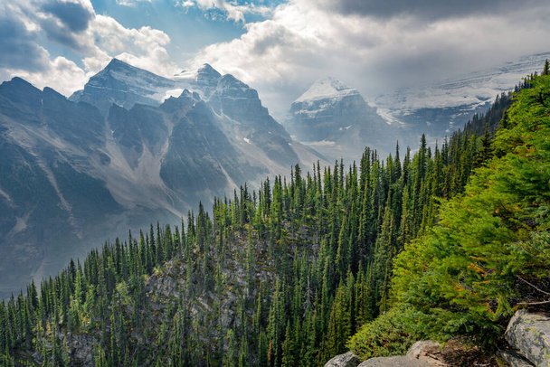 View of the trail to Big Beehive in Banff National Park, Alberta, Canada. Steep cliffs above alpine valley. Mountain range in summer haze. Mountain pines and dramatic clouds in the sky. - Zdjęcie, obraz