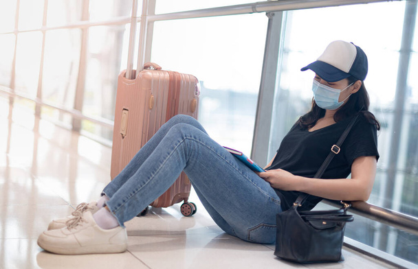 Ασιάτισσα γυναίκα που φοράει χειρουργική μάσκα αισθάνεται λυπημένη και καταθλιπτική για την χαμένη ή ακυρωμένη πτήση για επιβίβαση σε άλλο μέρος του αεροδρομίου, λόγω της επιδημίας Covid19. - Φωτογραφία, εικόνα