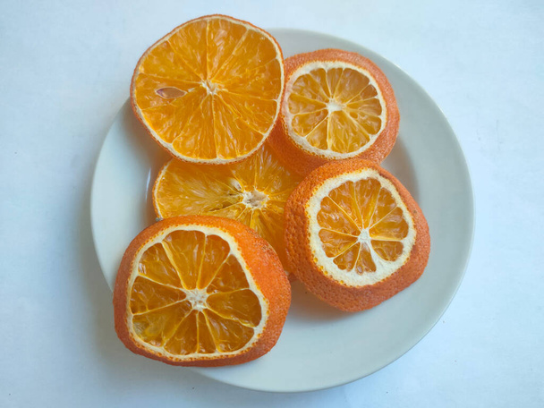 getrocknete Orangenscheiben auf einer weißen Untertasse auf hellem Hintergrund - Foto, Bild