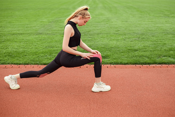 Girl stretches, prepares her body and muscles for a productive fitness workout. Flexible female sporty model on the city stadium. Image with copy space. - Fotoğraf, Görsel