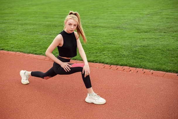 Girl stretches, prepares her body and muscles for a productive fitness workout. Flexible female sporty model on the city stadium. Image with copy space. - Φωτογραφία, εικόνα