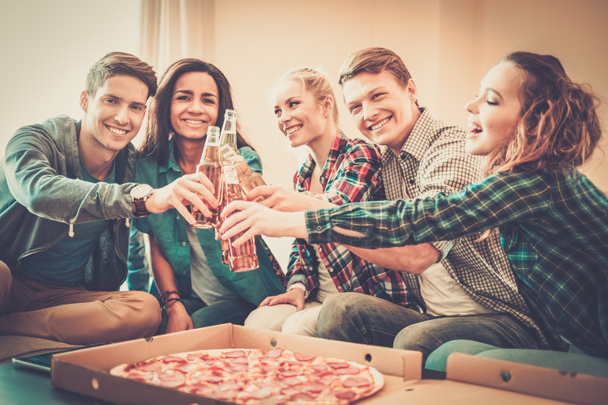 Group of young multi-ethnic friends with pizza and bottles of drink celebrating in home interior - Photo, Image