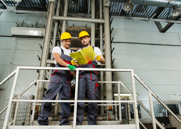 Due lavoratori con cappelli di sicurezza su un piano di lettura in fabbrica
  - Foto, immagini