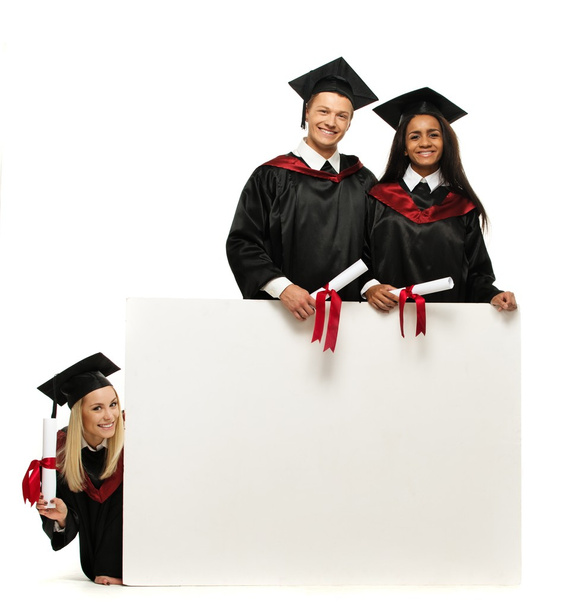 Grupo multiétnico de jóvenes estudiantes graduados con cartelera en blanco
 - Foto, imagen