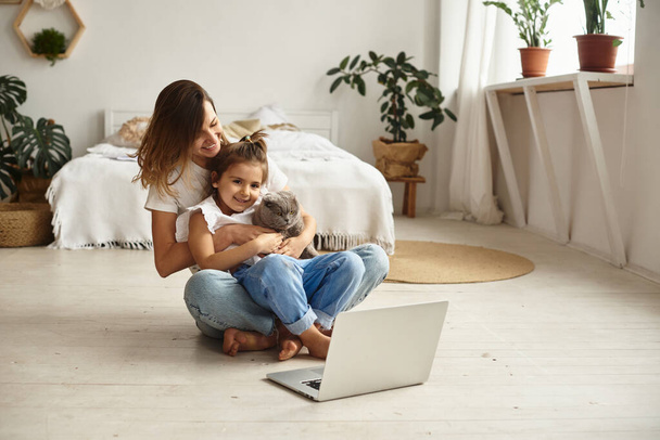 Daughter plays with mom and cat while mom works on computer - Fotoğraf, Görsel