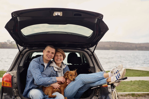 Young couple resting in the car with their dog. - Zdjęcie, obraz