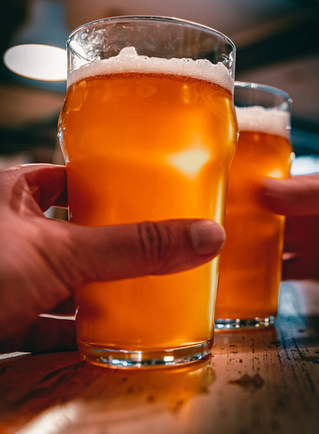 Close-up view of a two glass of beer in hand. Beer glasses clinking in bar or pub - Foto, immagini