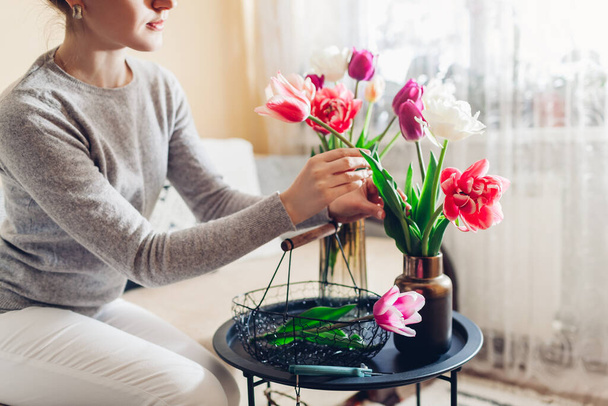 Woman arranges bouquet of tulips flowers at home using metal basket. Housewife taking care of coziness in apartment. Interior and decor - Фото, изображение