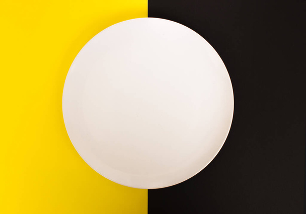 White empty plate on yellow and black background, top view, place for text - Fotó, kép