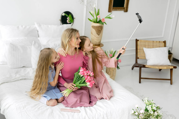 Dwie córki i matka robią sobie selfie przez telefon. Dziewczynki podarowały matce bukiet tulipanów i są fotografowane jako pamiątka. Słodkie i piękne dziewczyny. Dzień Matki. - Zdjęcie, obraz