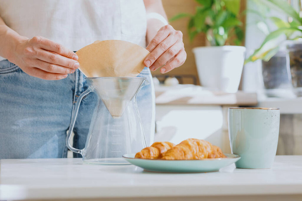 European woman brews coffee at home in her kitchen and enjoys her morning, good morning, caucasian woman makes coffee filter at home and enjoys her day off - Фото, изображение