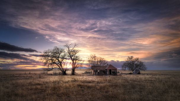 Antiga fazenda abandonada ao pôr do sol nos planos orientais do Colorado em uma cena rural. O céu está cheio de nuvens coloridas brilhantes. A paisagem rural é árida e árida. - Foto, Imagem