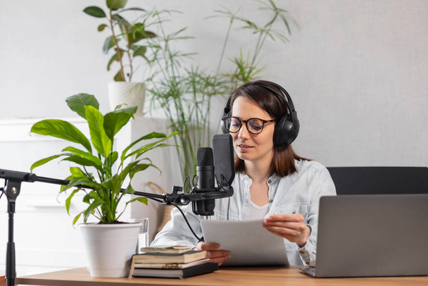 A fashionable European woman wearing headphones and a microphone records a podcast or radio show, a Caucasian woman creates audio content for her blog or podcast or records her voice for an audiobook - Foto, Bild