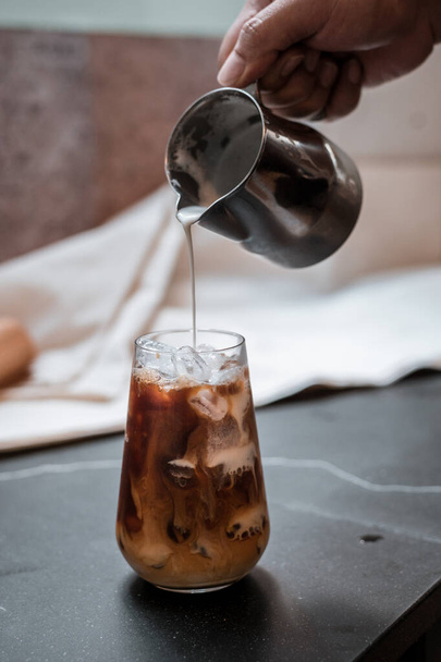 Бариста наливает молоко в стакан кофе со льдом - Фото, изображение