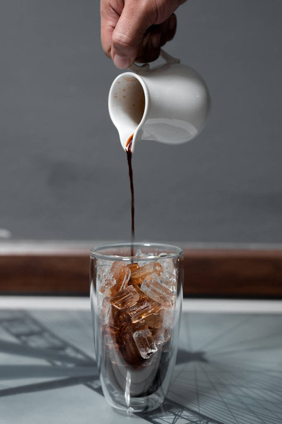 Barista pouring milk into a glass of iced coffee - Foto, afbeelding