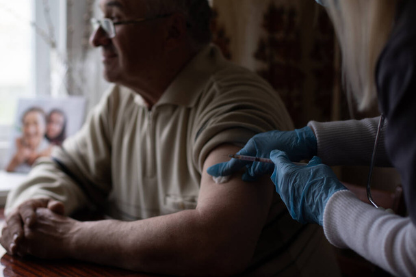 Lääkäri valmistelee rokotusrokotteen vanhuksille pitämällä ruiskua kotona - käsite kodin terveystarkastus senioreille sepelvaltimoviruksen covid-19 pandemian aikana - Valokuva, kuva
