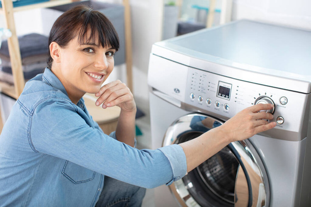 woman pressing button of washing machine in kitchen - Photo, image
