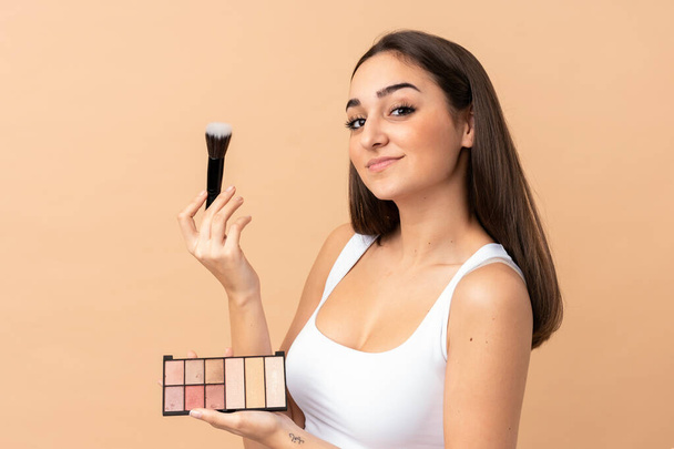 Junge kaukasische Frau isoliert auf beigem Hintergrund mit Make-up-Palette - Foto, Bild