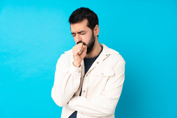 Young handsome man with white corduroy jacket over isolated blue background is suffering with cough and feeling bad - Foto, afbeelding