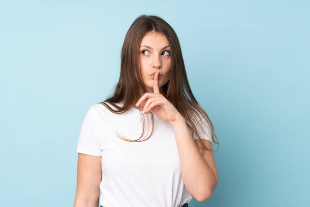 Teenager caucasian girl isolated on blue background showing a sign of silence gesture putting finger in mouth - Fotó, kép