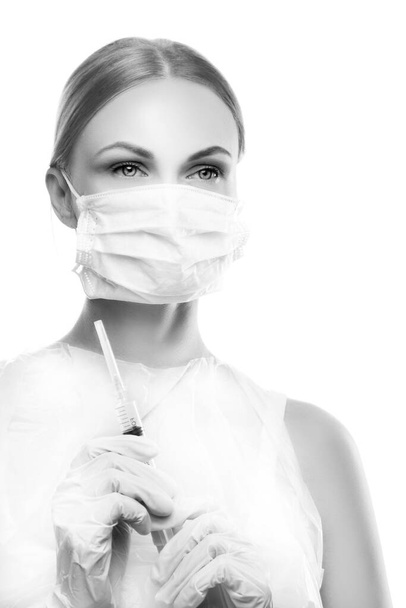 Όμορφη νεαρή γυναίκα γιατρός, νοσοκόμα, αισθητικός, οδοντίατρος πρόσωπο φορώντας προστατευτική μάσκα κρατήσει σύριγγα. Πορτρέτο στούντιο. Έννοια υγειονομικής περίθαλψης - Φωτογραφία, εικόνα
