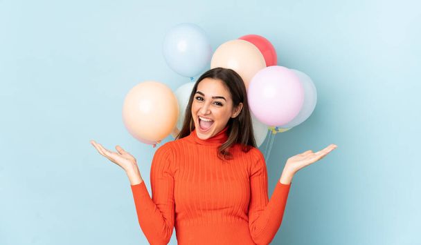 Young woman with many balloons isolated on blue background - Фото, изображение
