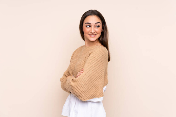 Young caucasian woman isolated on beige background with arms crossed and happy - Fotoğraf, Görsel