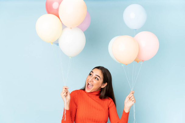 Young woman catching many balloons isolated on blue background - Foto, afbeelding