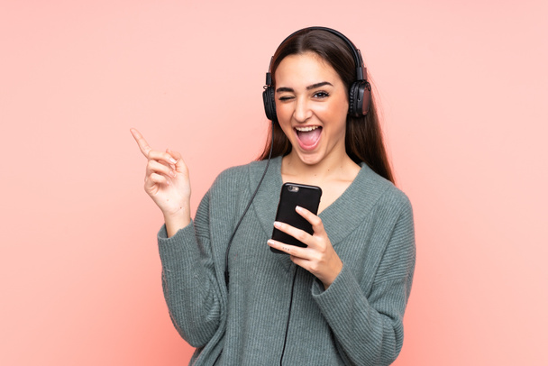 Young caucasian woman isolated on pink background listening music with a mobile and singing - Fotografie, Obrázek