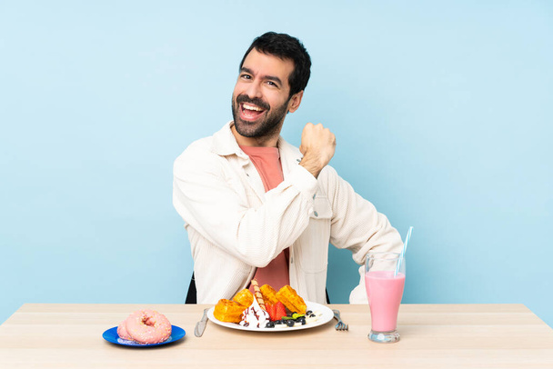 Человек за столом, завтракающий вафлями и молочный коктейль, празднующий победу - Фото, изображение