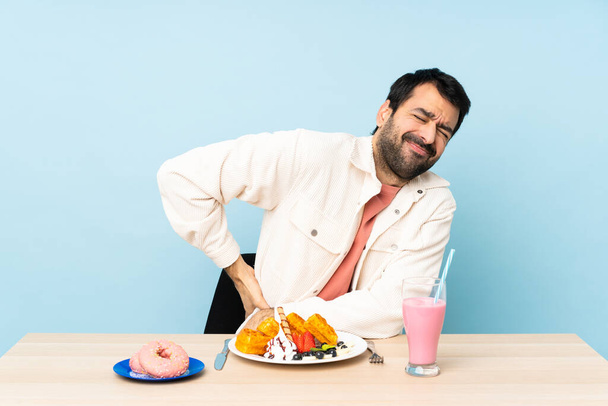Άνθρωπος σε ένα τραπέζι που τρώει βάφλες και ένα μιλκσέικ που υποφέρει από οσφυαλγία επειδή έκανε μια προσπάθεια - Φωτογραφία, εικόνα