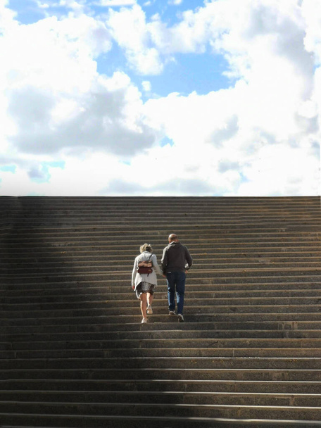 A back view of a lovely senior couple ascending wide long stairs to the cloudy sky - Valokuva, kuva