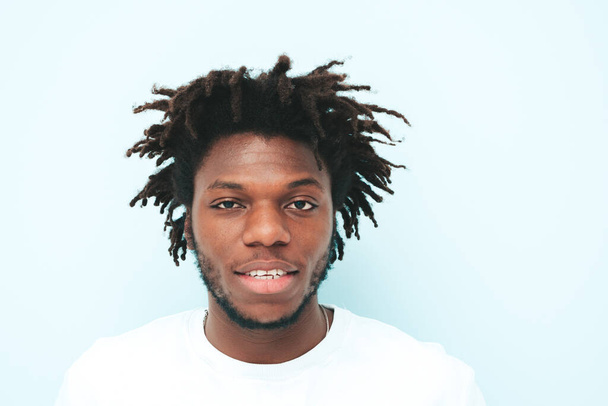 Portrait of handsome smiling hipster lambersexual model.Unshaven African man dressed in summer stylish clothes. Fashion male with dreadlocks hairstyle posing near light blue wall in studio - Φωτογραφία, εικόνα