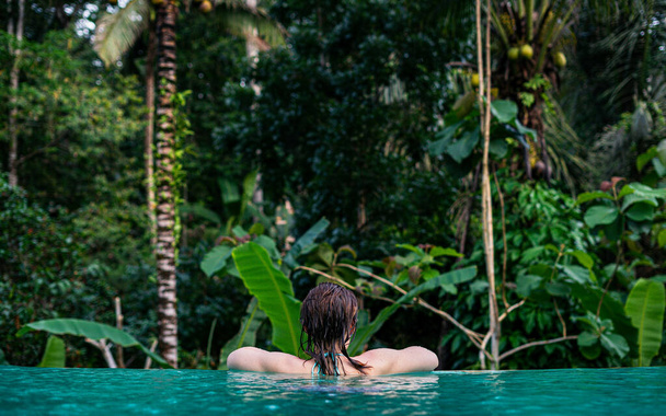 Μια νεαρή γυναίκα κολυμπά σε μια πισίνα και απολαμβάνει την όμορφη θέα της φύσης - Φωτογραφία, εικόνα