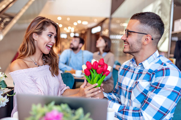 Attraktives Paar im Café. Mann schenkt seiner Freundin Blumen. Menschen, Liebe und Lebensstil-Konzept. - Foto, Bild