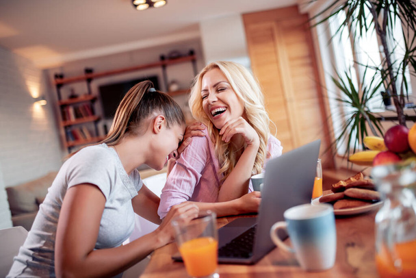 Two beautiful women enjoying at home and using laptop. - Foto, Imagen