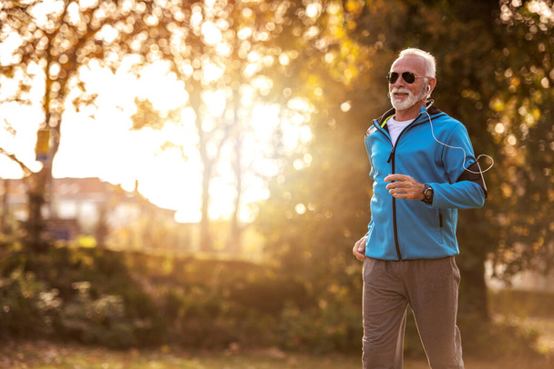 Senior mężczyzna jogging w jesiennym parku. Koncepcja zdrowego stylu życia. - Zdjęcie, obraz