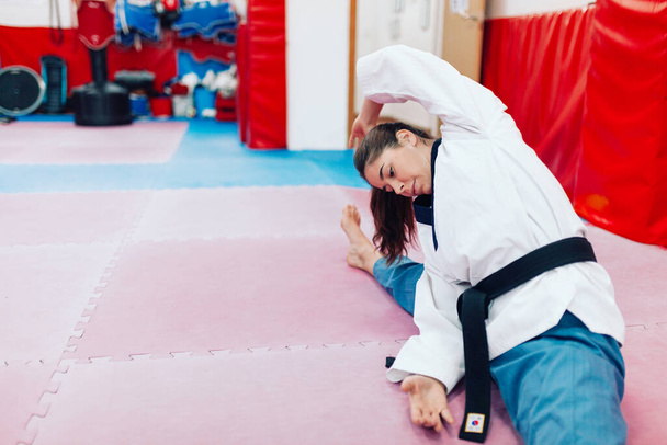 Mujer joven estirándose en un dojo usando taekwondo dobok - Foto, Imagen