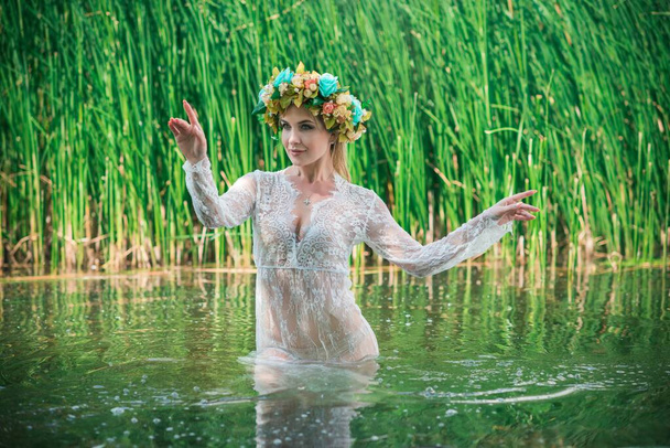 Uma fabulosa, ninfa lago em longo vestido de renda branca e grinalda. Fotografia artística, cena misteriosa. Bruxa Europeia. Conto de fadas - Foto, Imagem