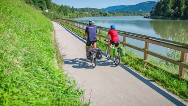 Ampio angolo sinistro panning shot di un uomo e di una donna in bicicletta lungo la bella pista ciclabile Drava in Muta Slovenia durante il giorno - Filmati, video