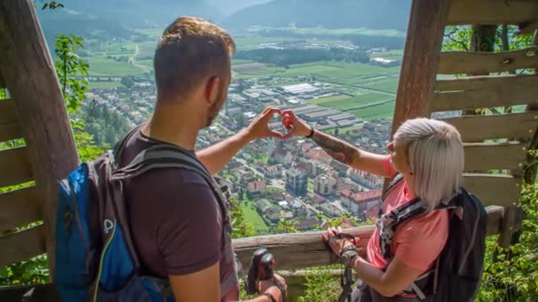 Couple makes a heart with their hands. Overlooking beautiful scenery in the background. Green window, Slovenia - Footage, Video