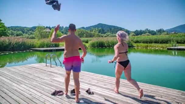 Paar rennende richting rand van het buitenzwembad gooien van kleding in de lucht. Langzame beweging - Video