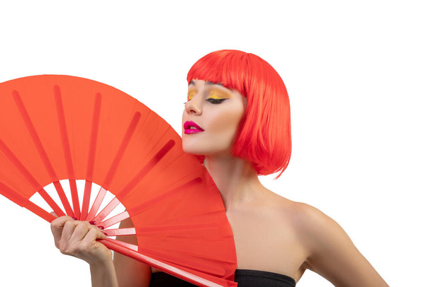 Kırmızı fanı tutan kısa kırmızı peruk takan güzel bir kız beyaz arka planda izole edilmiş. - Fotoğraf, Görsel