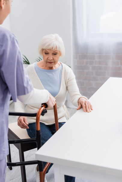 enfermera dando caminantes médicos a la mujer mayor sentada en la cocina - Foto, Imagen