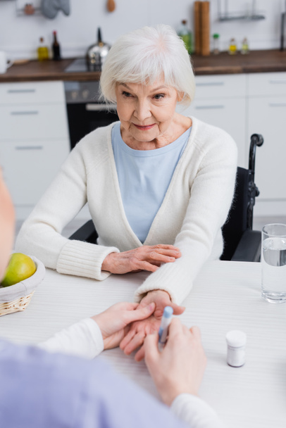 elderly woman looking at nurse doing injection of insulin on blurred background - Photo, Image