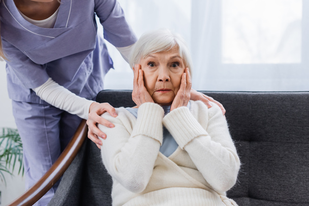 mulher idosa, doente de amnésia, de mãos dadas perto do rosto, enquanto a assistente social toca os ombros - Foto, Imagem