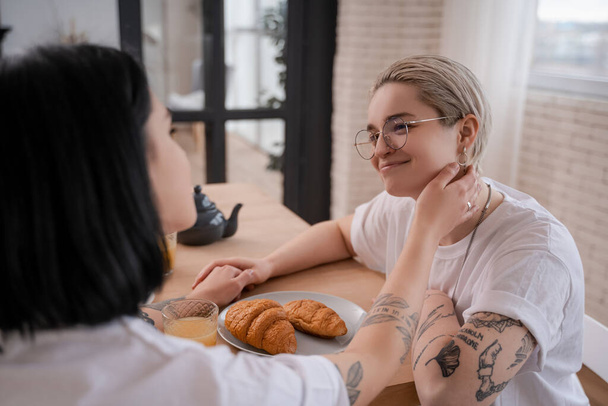 happy lesbian couple holding hands and looking at each other in kitchen  - Foto, afbeelding