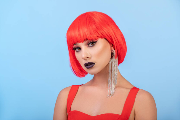 Portrait of Pretty woman in red wig over blue background. long earring - Photo, Image