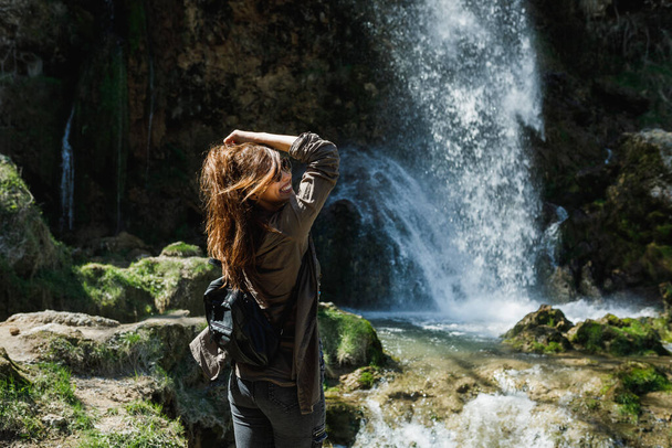 A smiling young woman enjoying the view of the beautiful waterfall. - 写真・画像