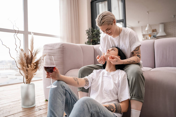 tattooed woman looking at girlfriend with glass of red wine  - Photo, image